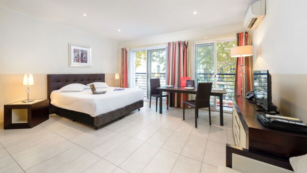 A hotel room with a bed, desk, chair, and a window with curtains. - Appart’Hôtel La Villa Carnot Cannes (Cannes)
