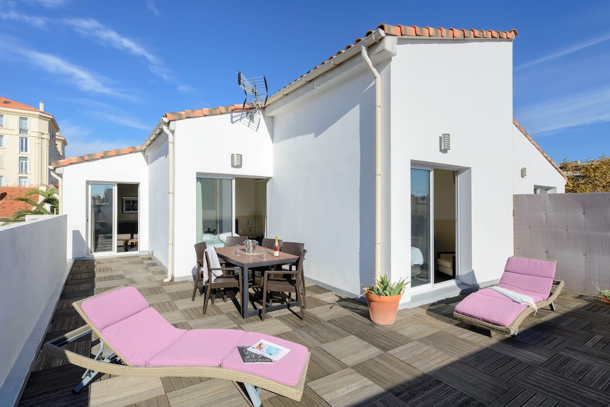 A rooftop terrace with a dining area, lounge chairs, and a potted plant.