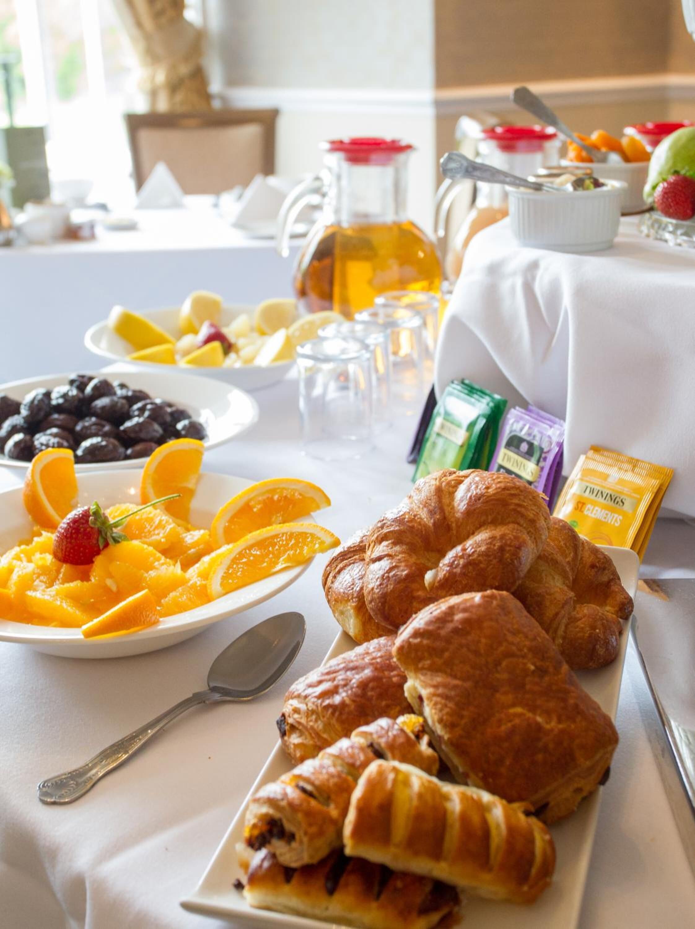 A breakfast table with croissants, fruit, and a coffee pot.