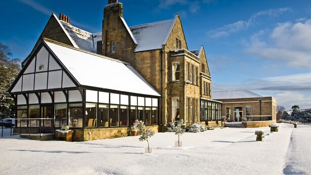 A large, historic building with a prominent gabled roof and large windows, surrounded by snow. - Classic Lodges Grinkle Park Easington (Saltburn-by-the-Sea)