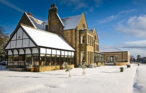 A large, historic building with a prominent gabled roof and large windows, surrounded by snow. - Classic Lodges Grinkle Park Easington (Saltburn-by-the-Sea)