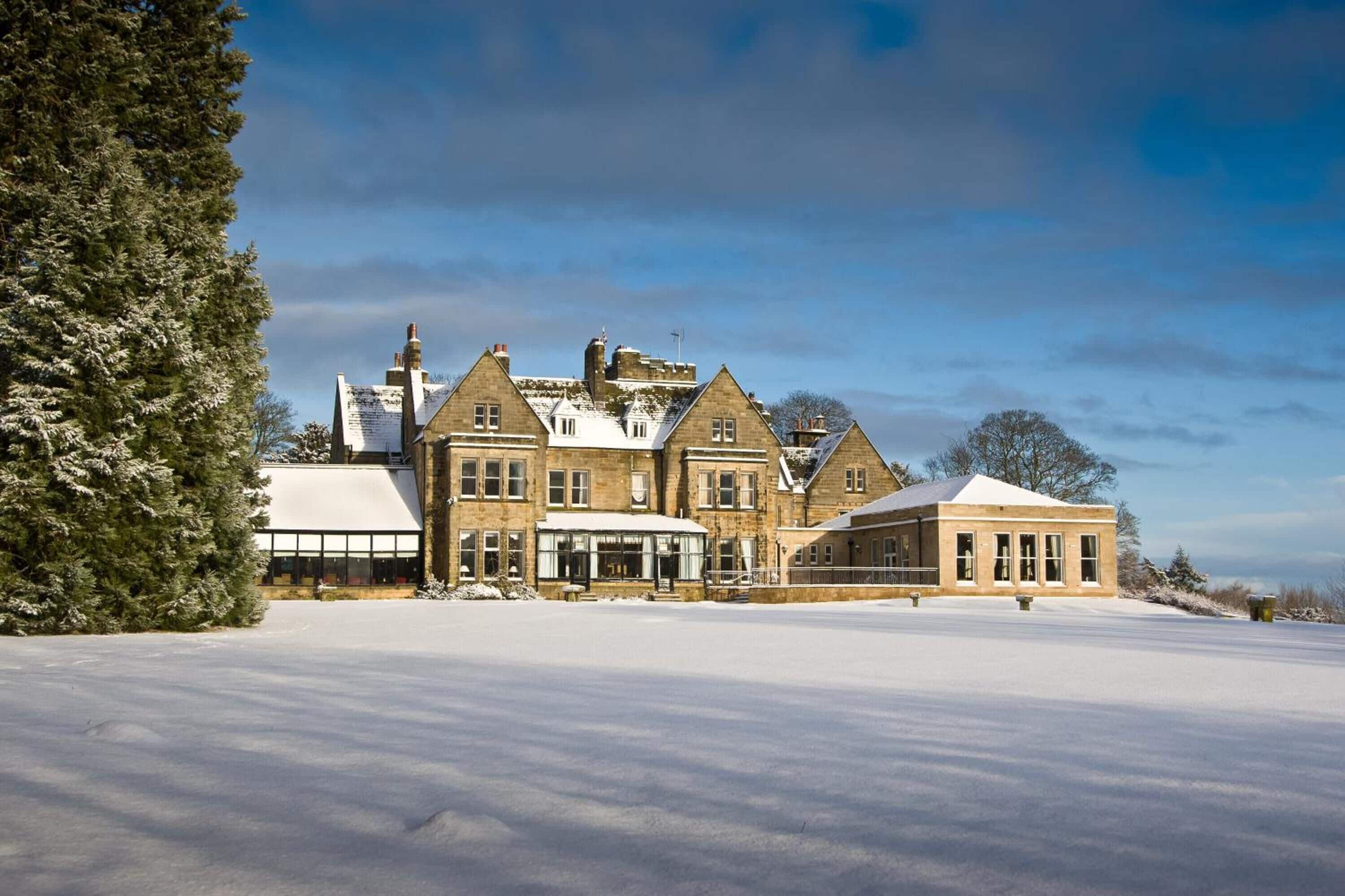 A large, historic building with multiple wings and a snow-covered landscape.