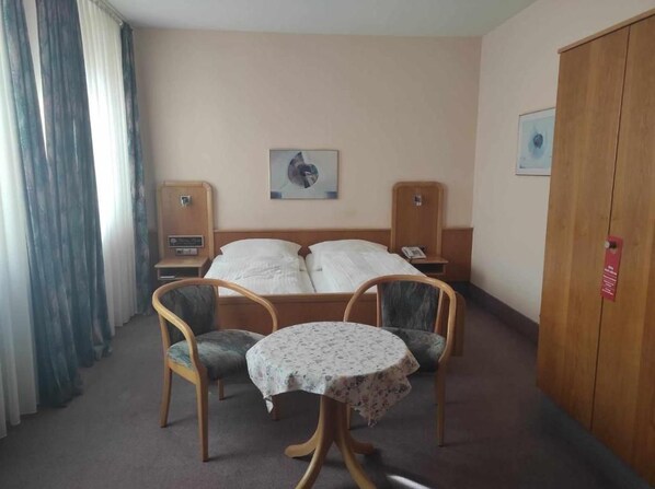 Ein Hotelzimmer mit einem Bett, zwei Stühlen, einem kleinen Tisch, einem Schrank und einem Nachttisch mit einem Radio.
