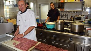 Uma cozinha com um chef cortando carne e outra pessoa ao fundo.
