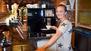 Máquina de café com interface digital, uma chávena de café e uma pessoa vestindo uma camisola com padrão de estrelas.