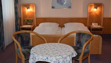 A hotel room with a double bed, two bedside tables with lamps, a small table with a floral tablecloth, and two chairs.