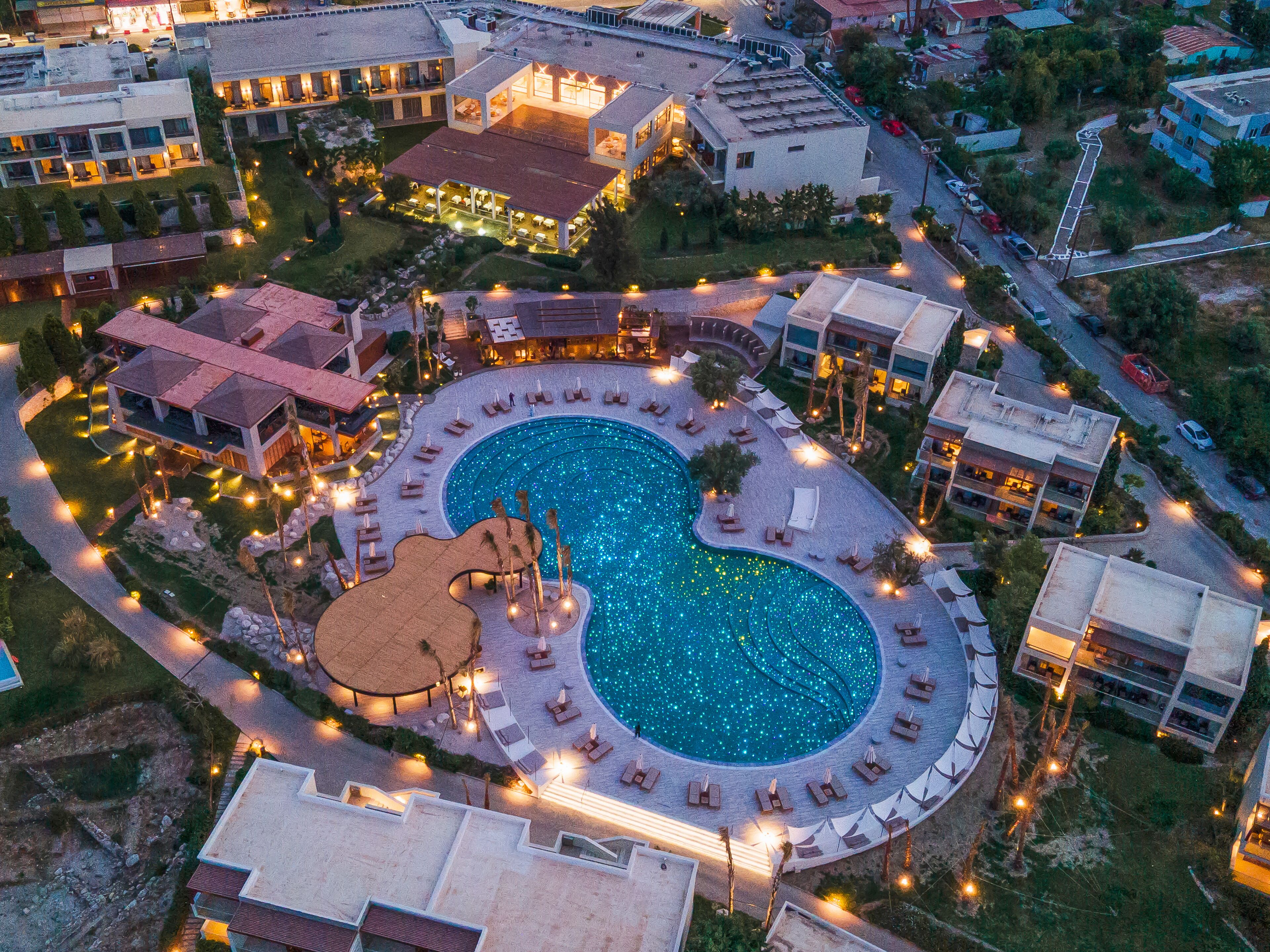 Vista aérea de un complejo turístico con una gran piscina, varias edificaciones y senderos bien iluminados.