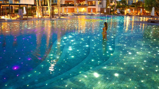 A nighttime swimming pool with starry sky, palm trees, and modern buildings in the background. - Port Royal Villas & Spa (Rhodes)