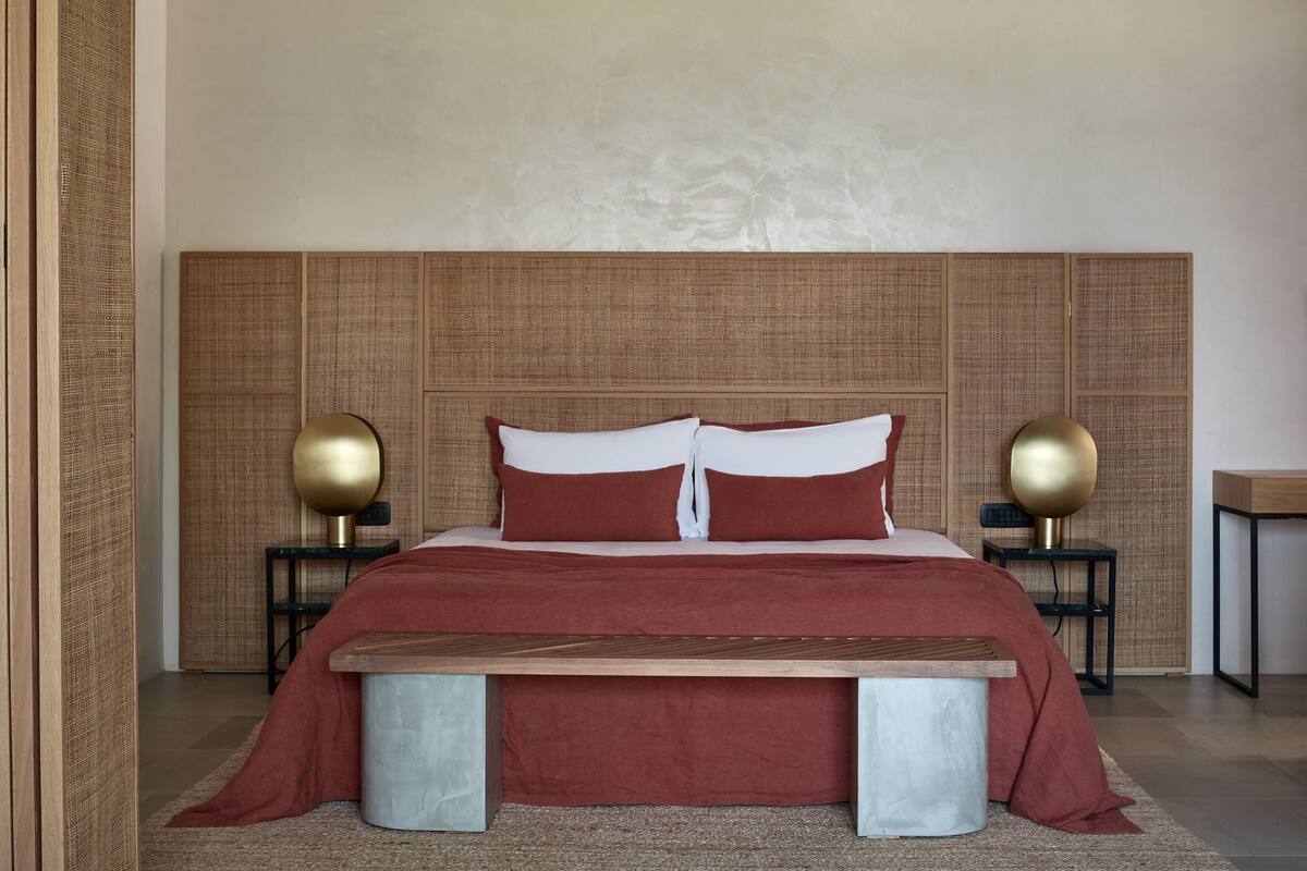Une chambre à coucher avec un grand lit, deux tables de chevet avec des lampes, un banc en bois et une tête de lit à motifs.