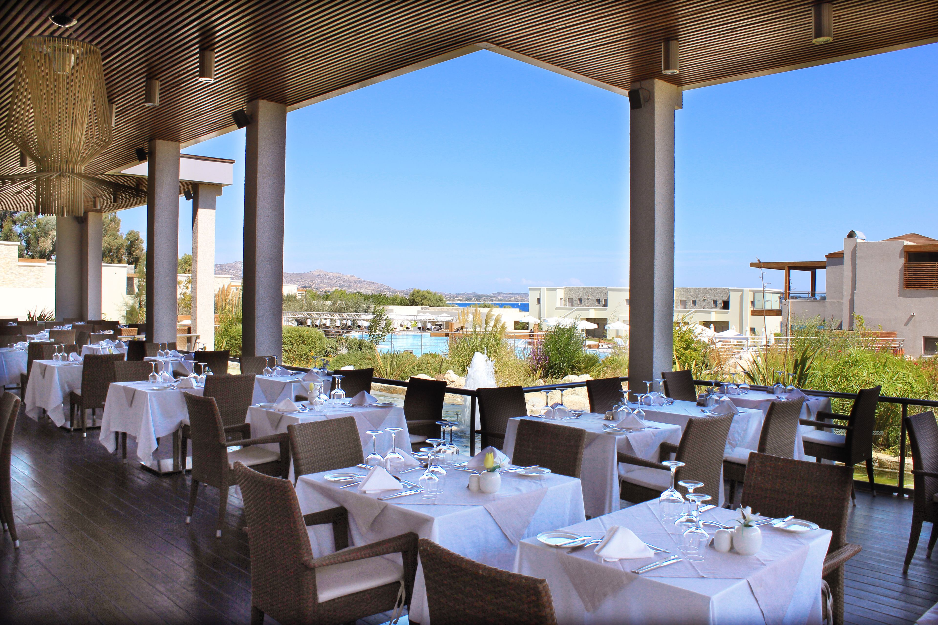 An outdoor dining area with tables set for a meal, overlooking a pool and buildings.