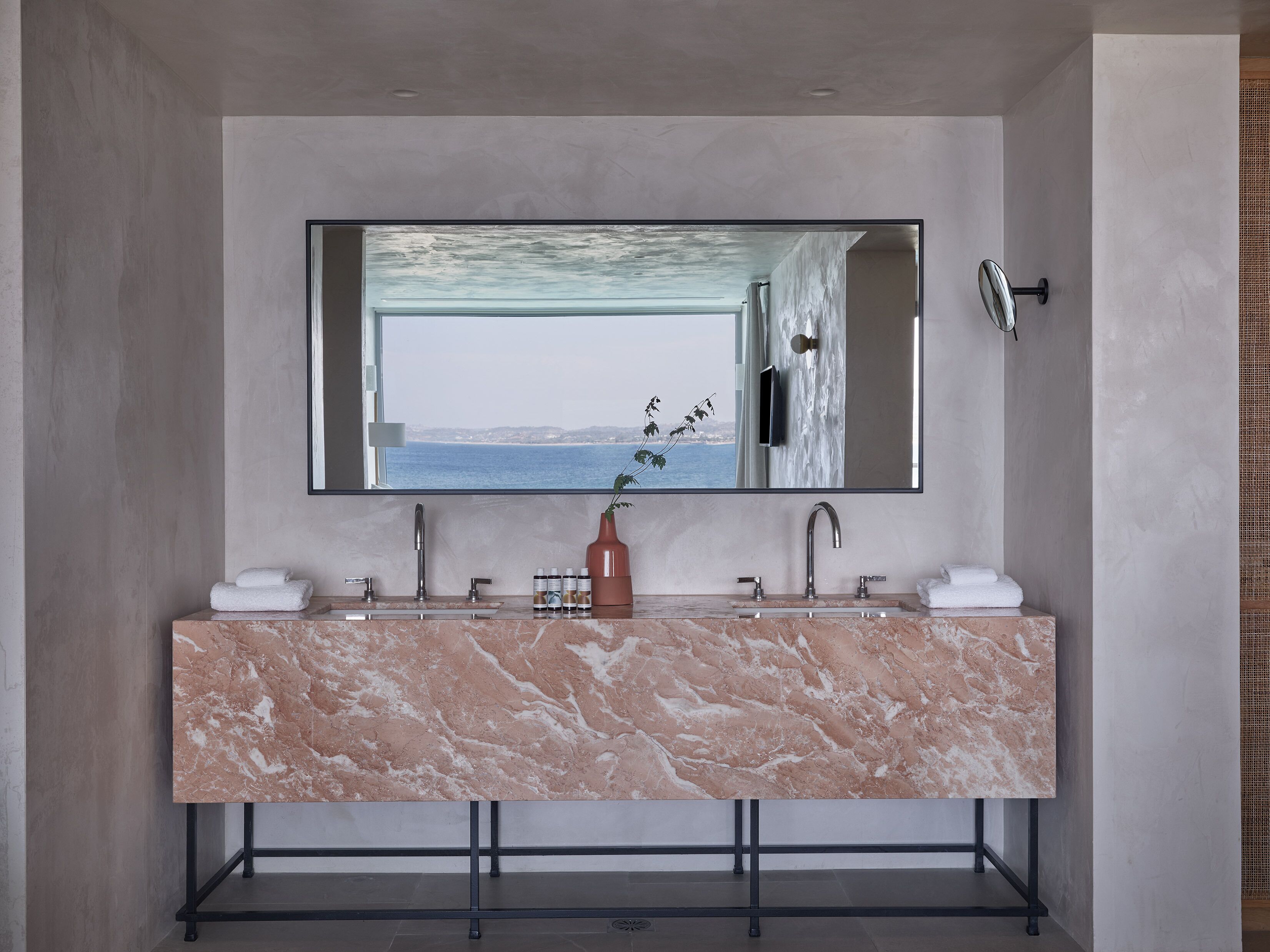 Un bagno con un grande specchio, un lavabo in marmo e vista sul mare.