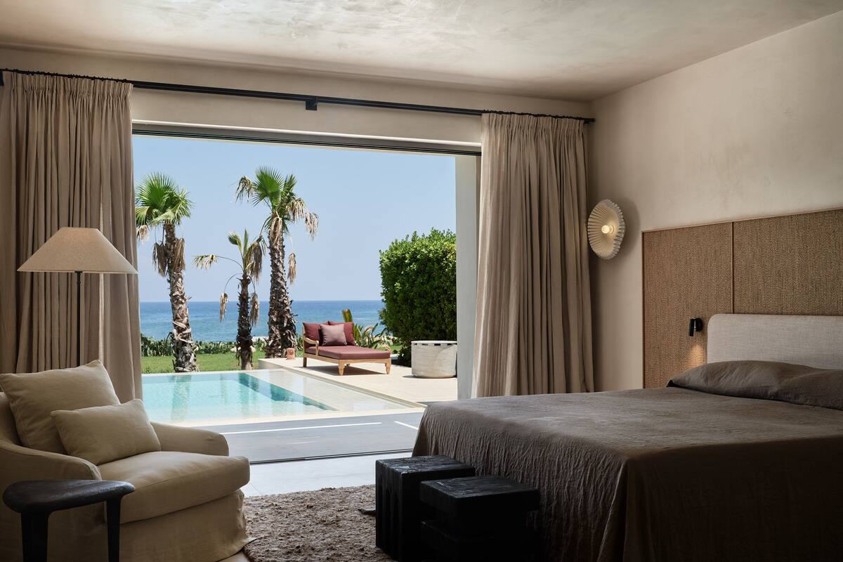 Une chambre avec un grand lit, un canapé, une petite table et une vue sur l’océan par une porte coulissante.