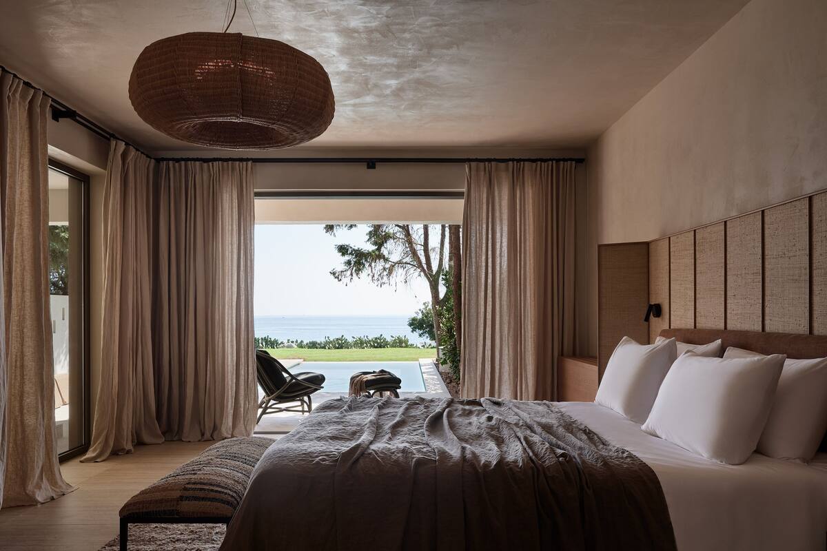 Une chambre avec un grand lit, une vue sur la mer et un luminaire suspendu au plafond en osier.