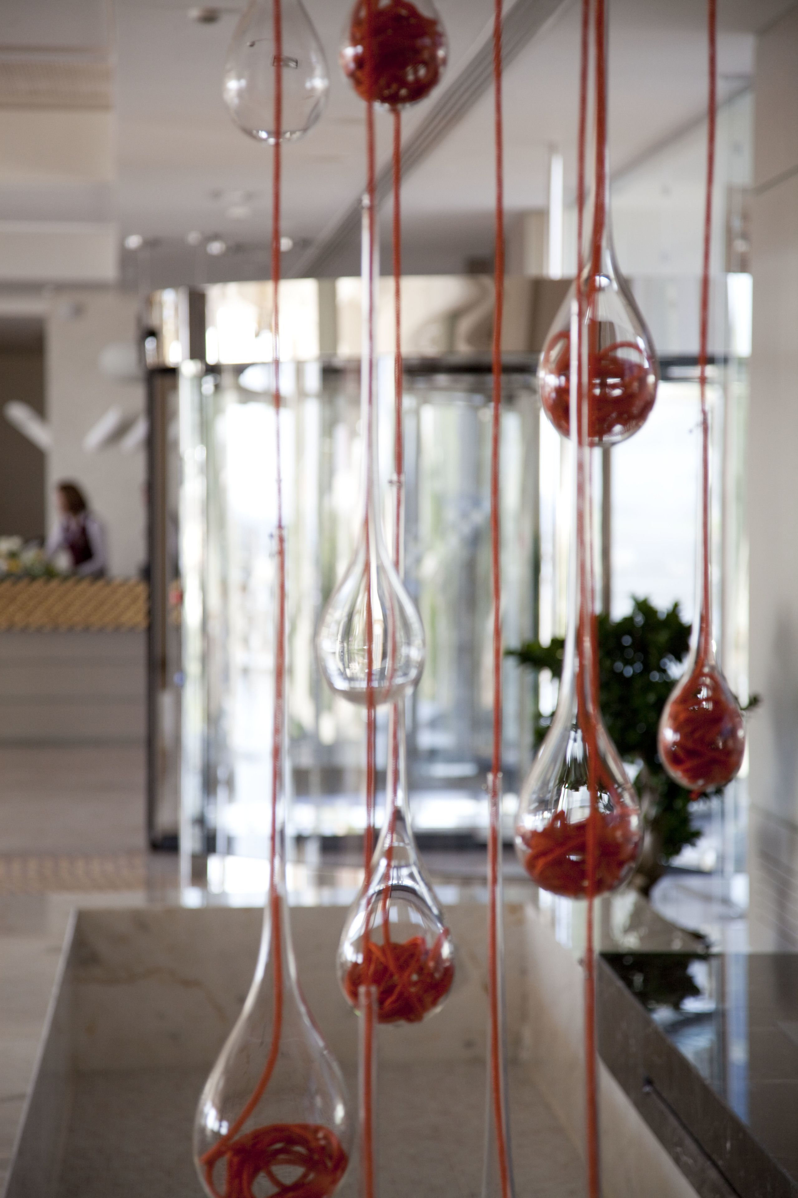 Glasvaser hänger ned från taket, dekorerade med röda snören, i en modern entréhall med en reception i bakgrunden.
