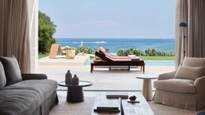 A modern living room with a large window offering a view of the ocean. - Port Royal Villas & Spa (Rhodes)
