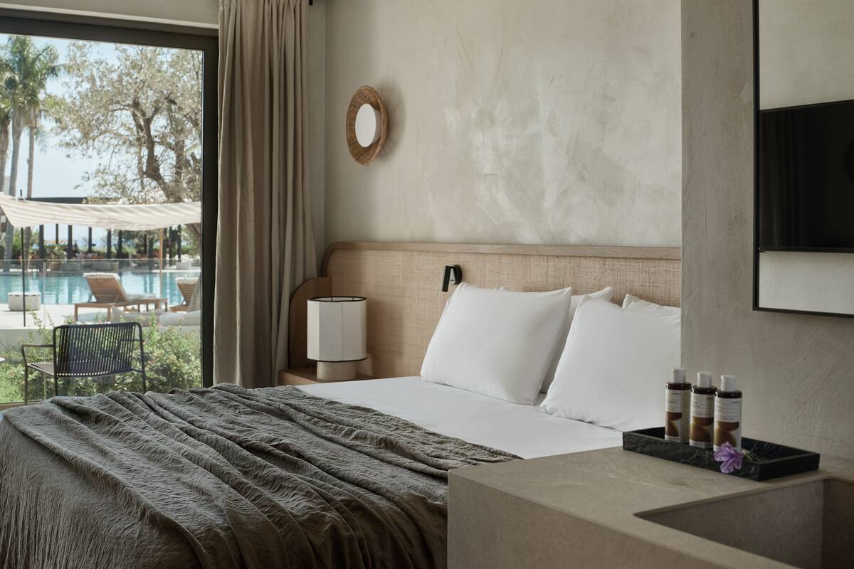 Une chambre d’hôtel avec un lit, une table de chevet avec une lampe, une vue sur une piscine extérieure et un miroir fixé au mur.