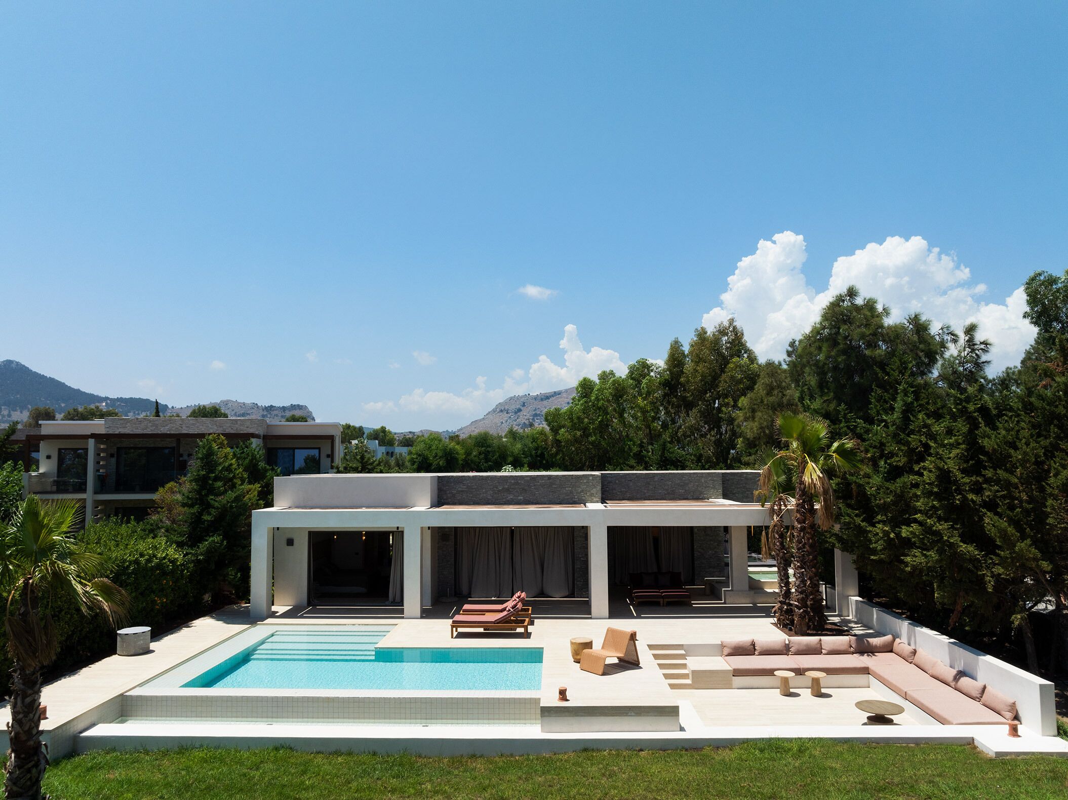 A modern house with a swimming pool, outdoor seating, and a view of the mountains.