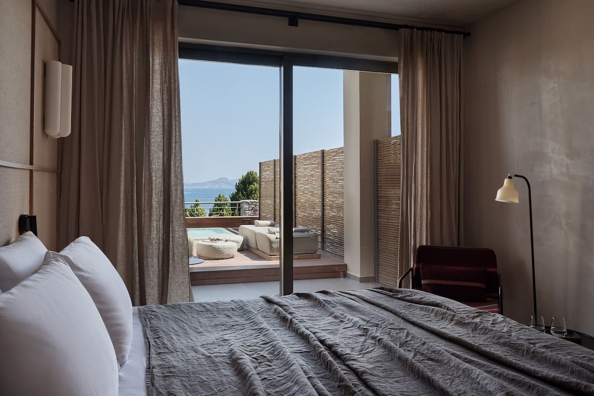 Une chambre d’hôtel avec un lit, un bureau, une chaise, une lampe et une vue sur la mer.
