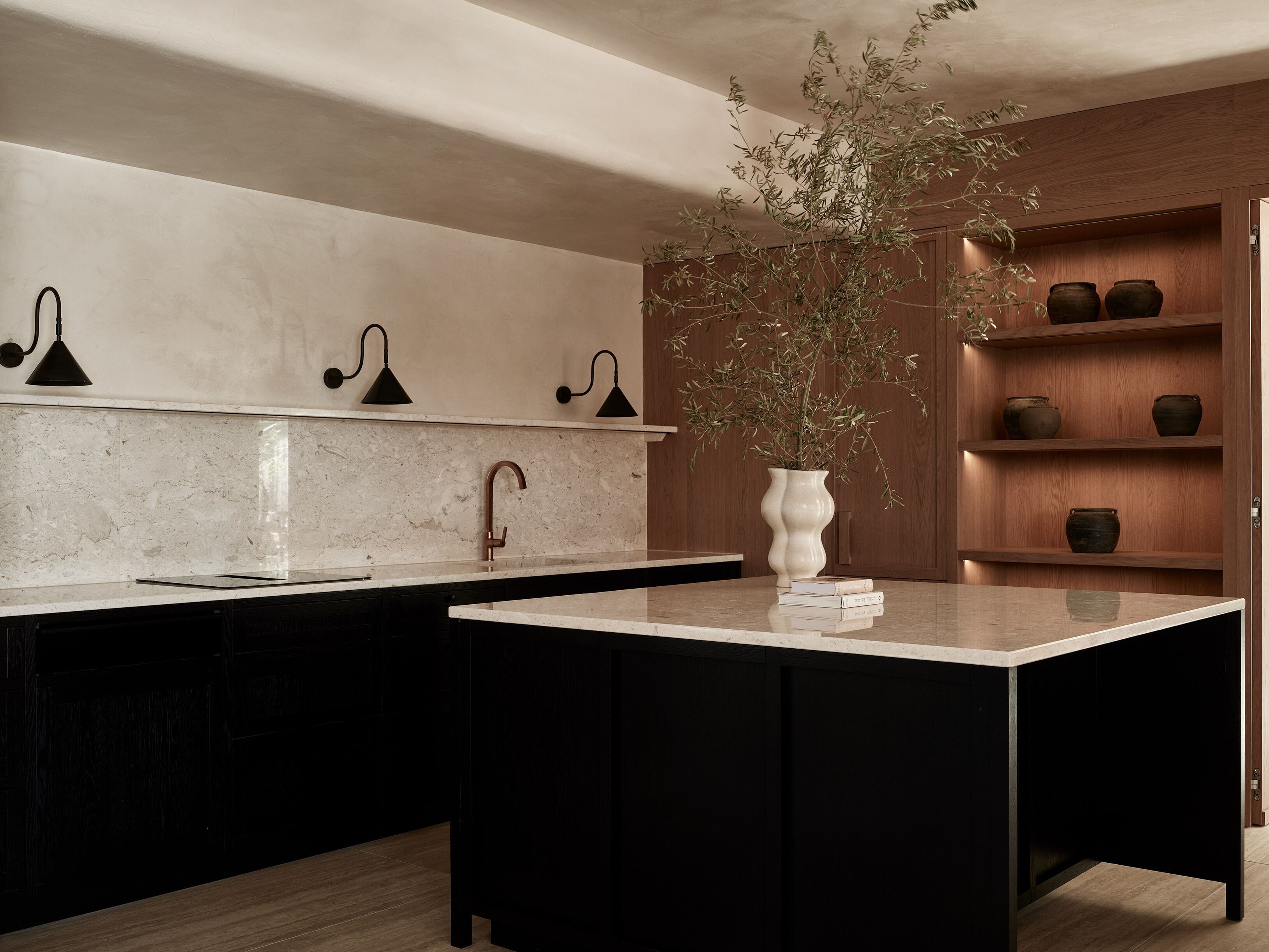 Una cocina moderna con encimera de mármol, armarios negros y un jarrón blanco con una planta.