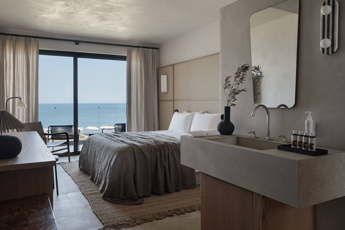 Une chambre d’hôtel moderne dotée d’un grand lit, d’un bureau, d’une salle de bain avec un miroir et des articles de toilette, et offrant une vue sur l’océan.
