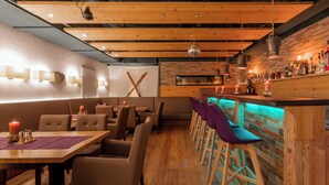 A restaurant with wooden ceiling beams, a bar area with stools, and a seating arrangement with tables and chairs. - AlpenParks Hotel Maria Alm (Maria Alm am Steinernen Meer)