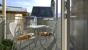 A screened balcony with a table and chairs, a bottle, and a view of a building with a clock tower. - AlpenParks Hotel Maria Alm (Maria Alm am Steinernen Meer)