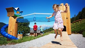A wooden deck with a rope bridge, a blue slide, and a wooden structure with a bird design. - AlpenParks Hotel Maria Alm (Maria Alm am Steinernen Meer)