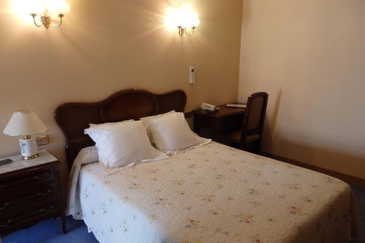 Ein Hotelzimmer mit einem Bett, einem Nachttisch, einem Schreibtisch und zwei Wandlampen.