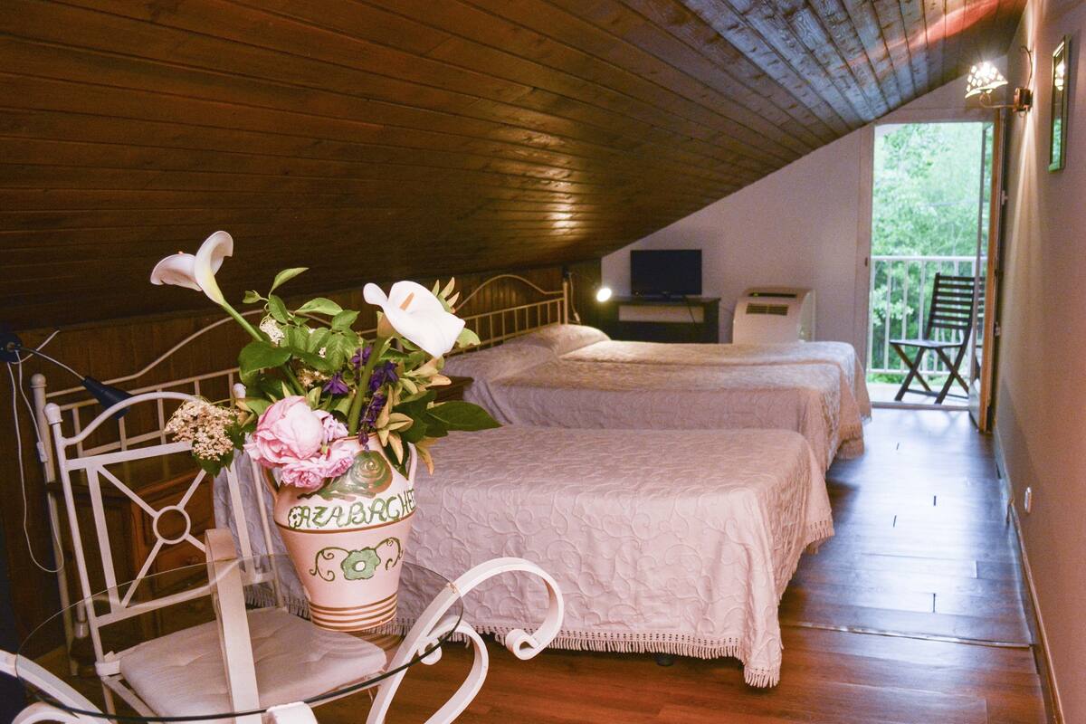Ein gemütliches Schlafzimmer im Dachgeschoss mit zwei Betten, einer Holzbalkendecke und einem Balkon mit einem Stuhl.