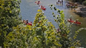 Een rivier omgeven door weelderige begroeiing, met mensen die kajakken en op de oevers staan.