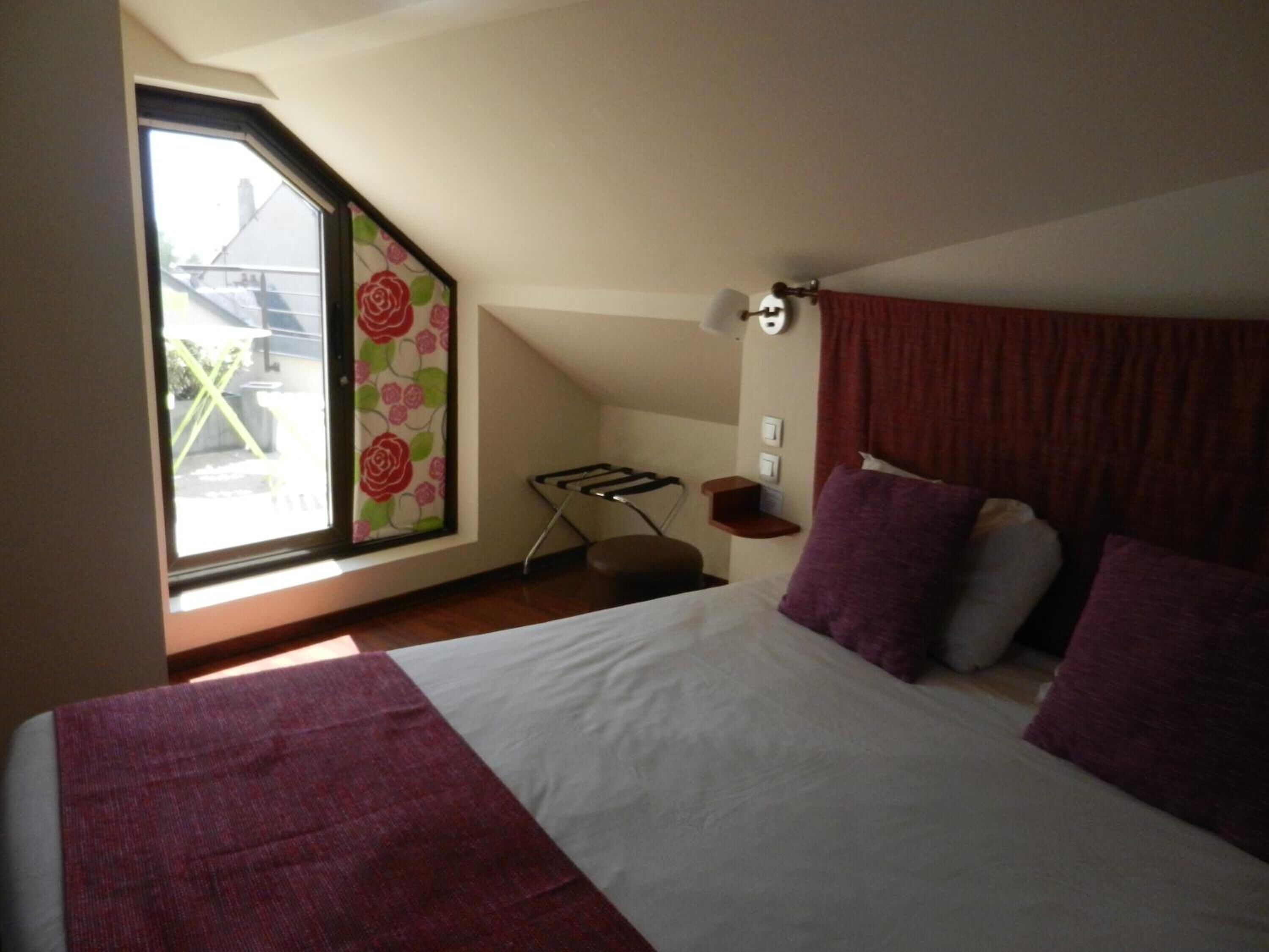 A bedroom with a large bed, a window with a view, a small table, and a wall-mounted light.