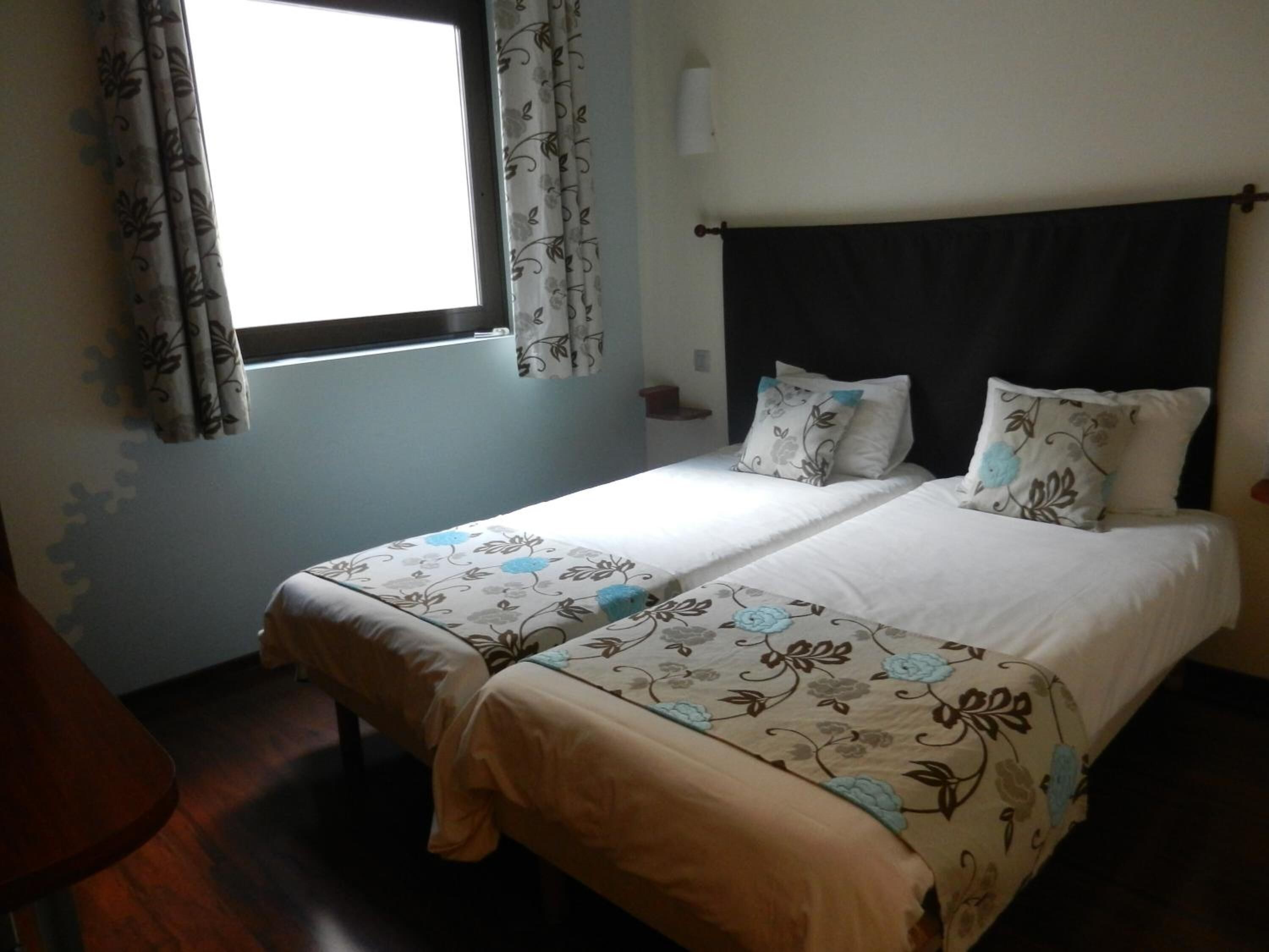 A double bed with floral bedding, a window with curtains, and a dark headboard.