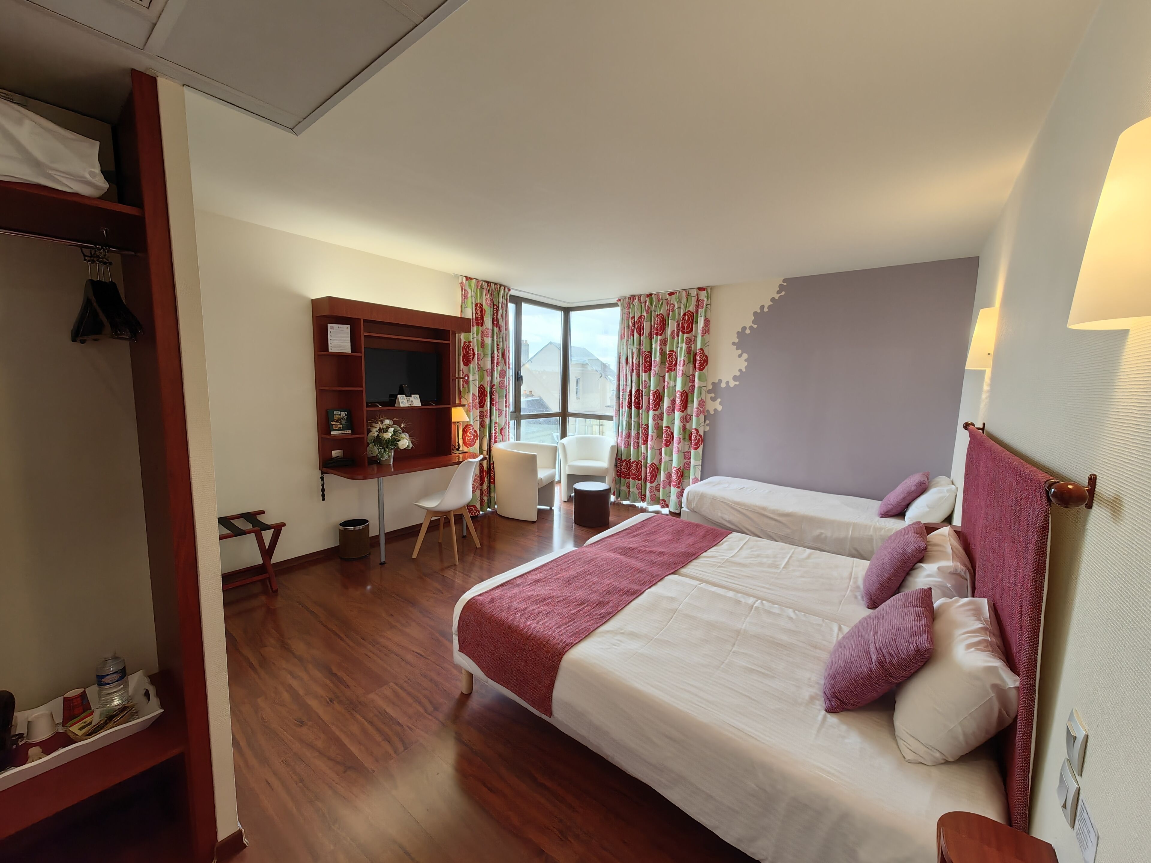 A hotel room with two beds, a desk, a chair, a mirror, and a window with curtains.