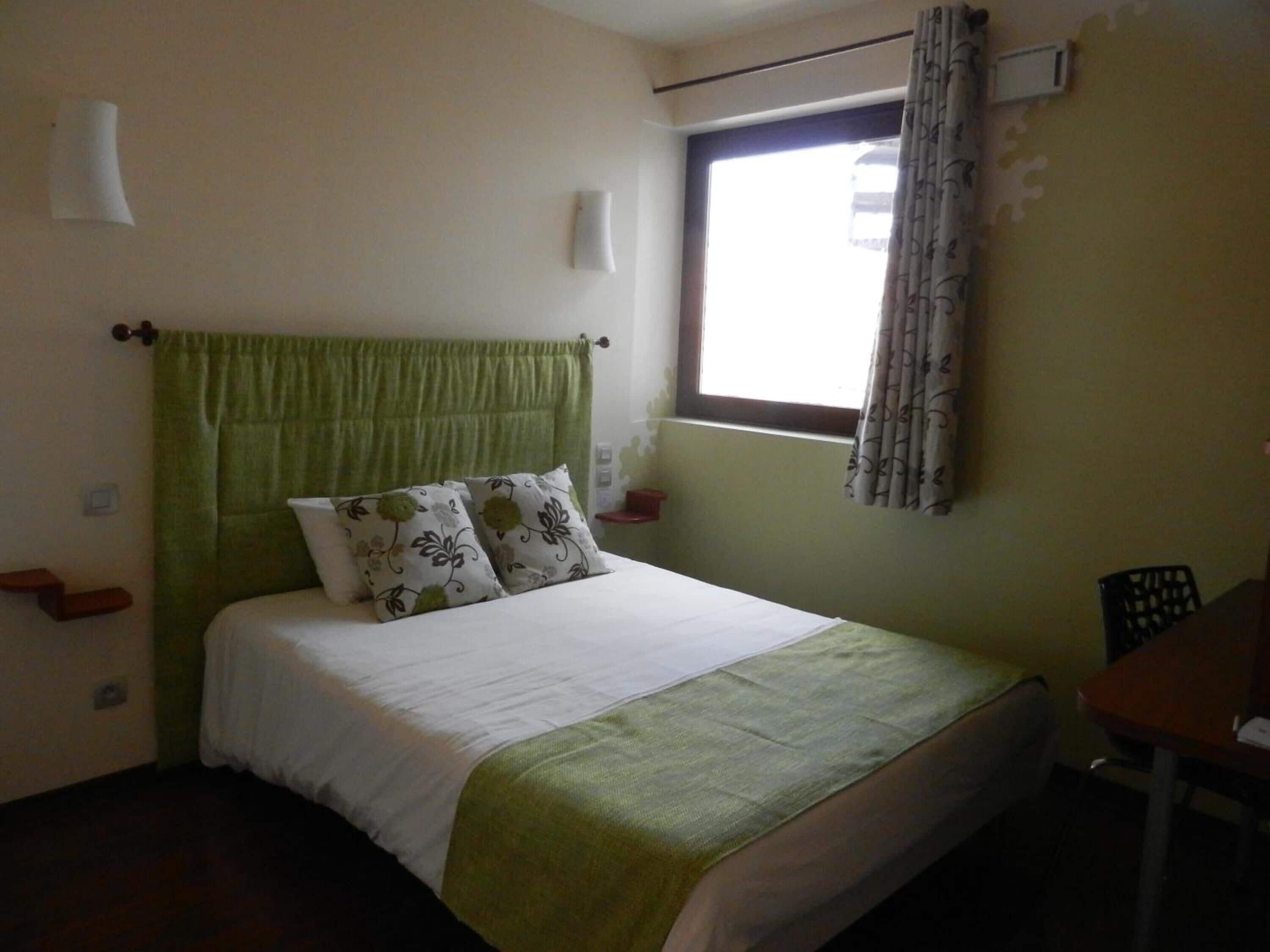 A bedroom with a bed, a window with curtains, a bedside table, and a chair.