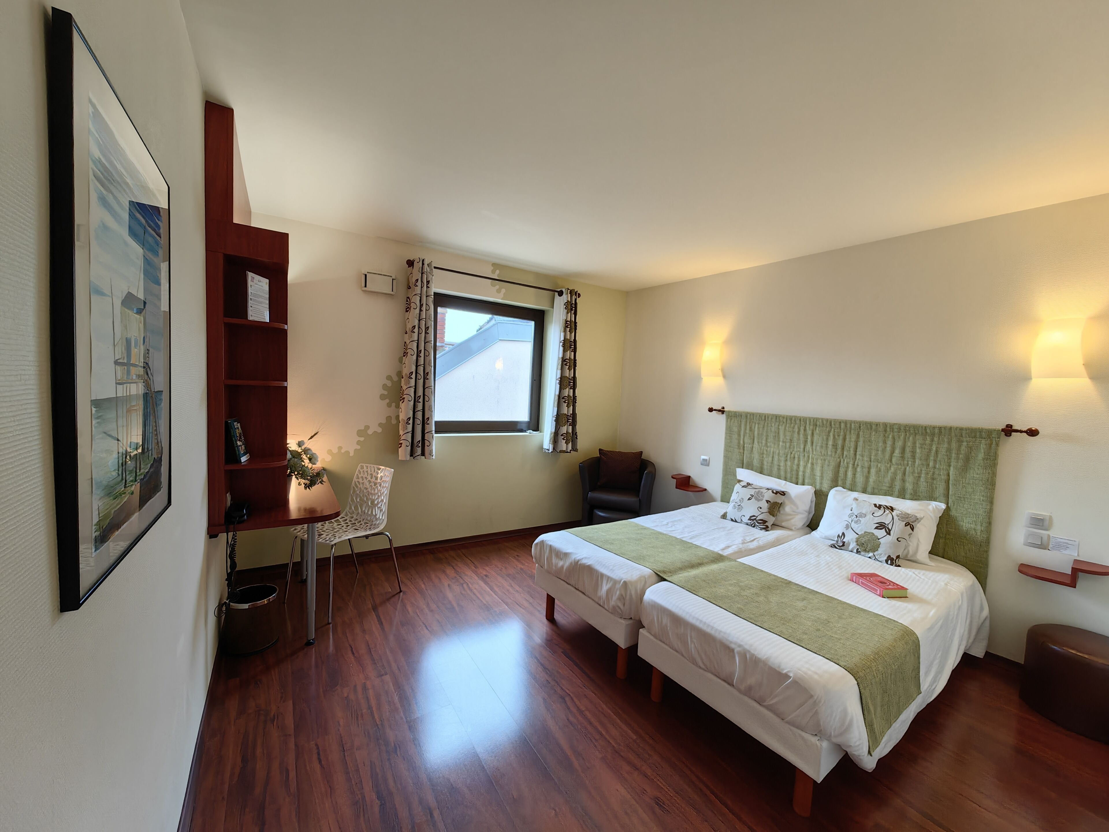 A hotel room with two beds, a desk, a chair, a bookshelf, and a window.