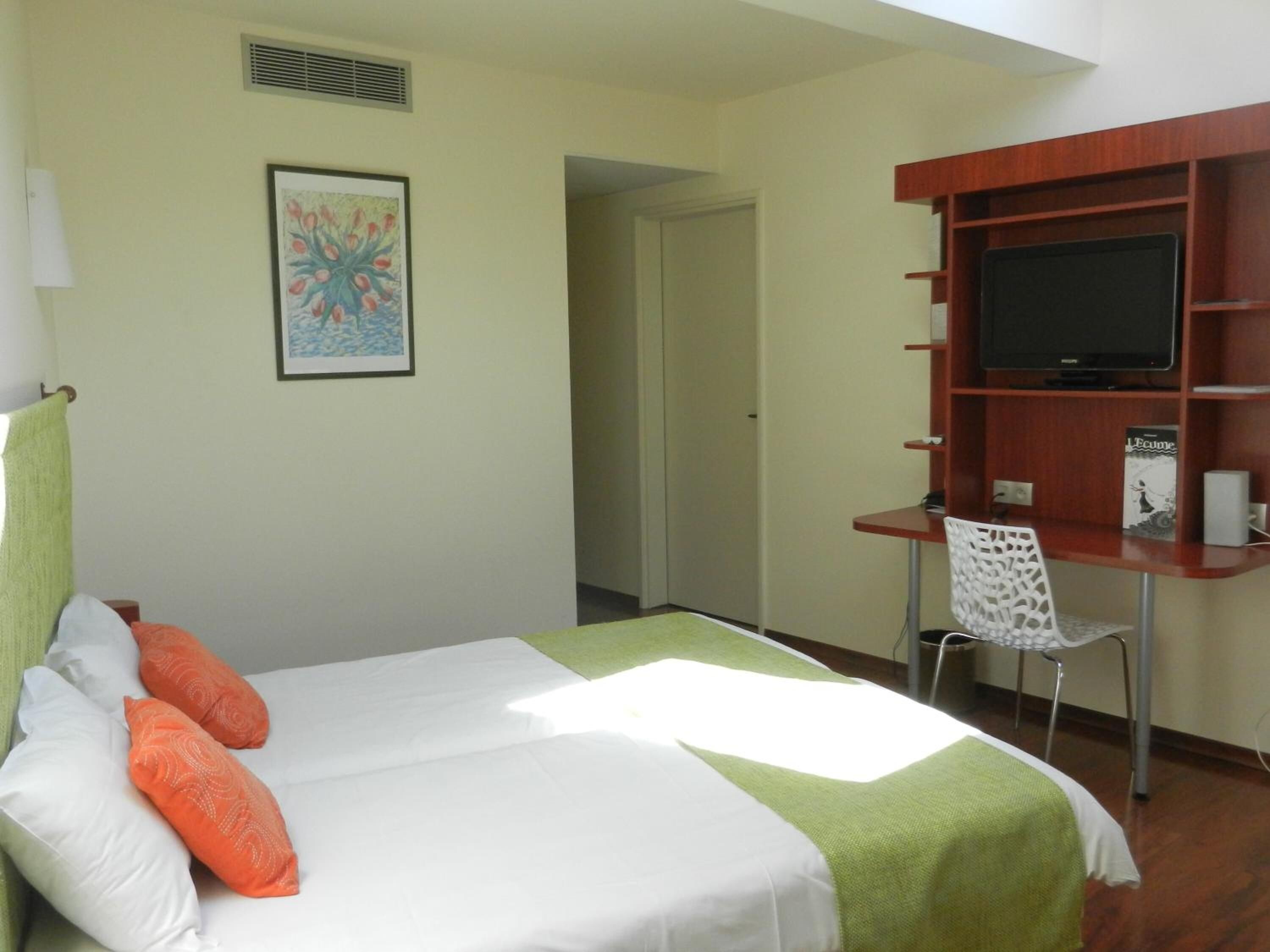 Habitación de hotel con cama, escritorio, silla, televisor y un cuadro en la pared.
