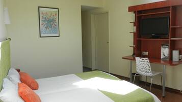 Habitación de hotel con cama, escritorio, silla, televisor y un cuadro en la pared.