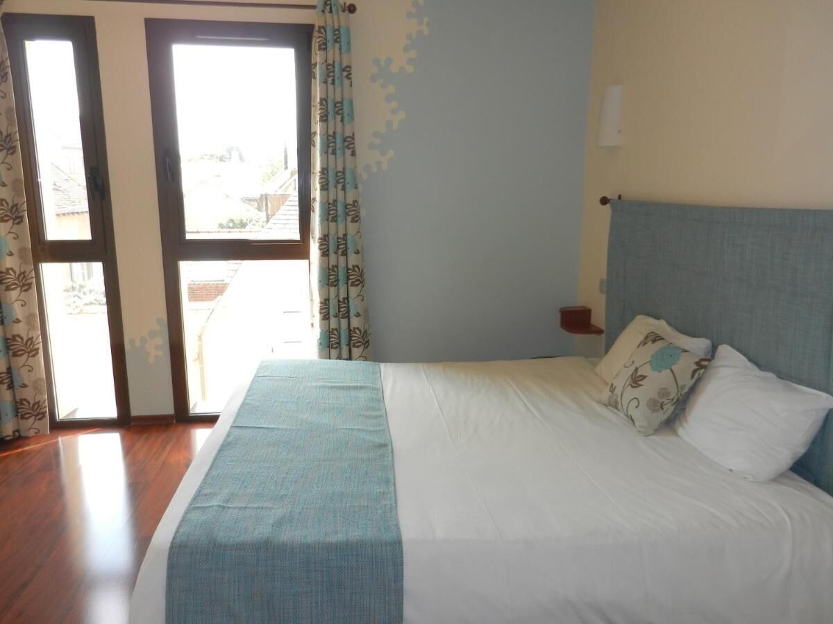 A bedroom with a bed, curtains, a nightstand, and a view through a door.