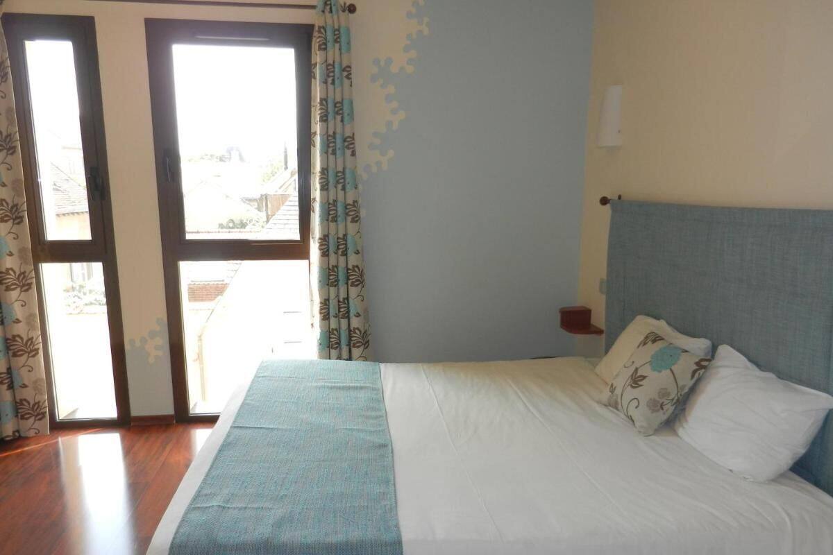 A bedroom with a bed, curtains, a nightstand, and a view through a door.