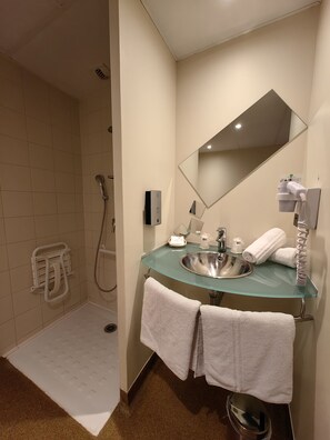 A modern bathroom with a glass sink, a large mirror, a shower, and two towels hanging on the wall.