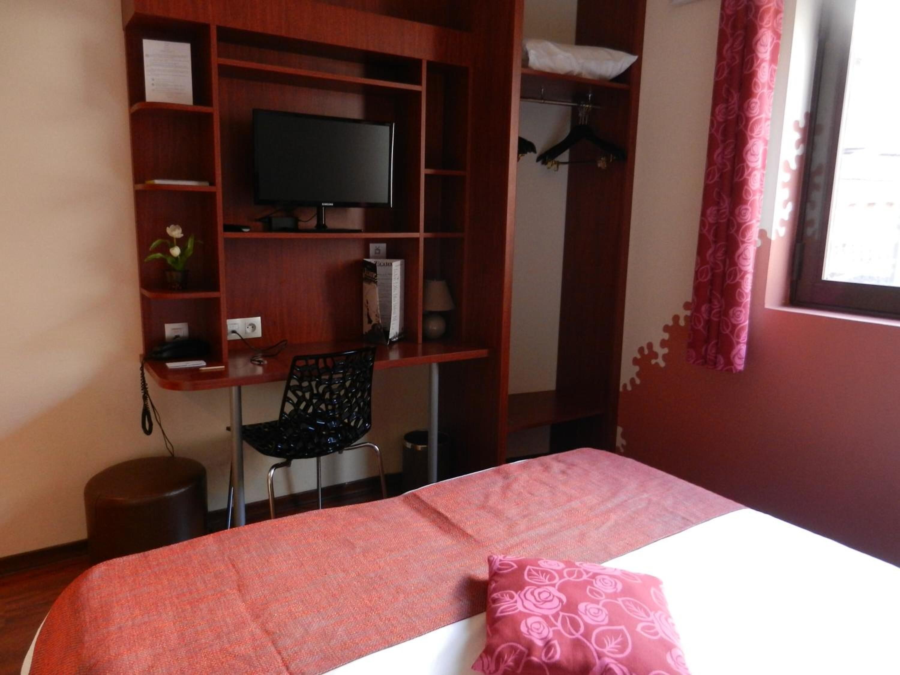 A bedroom with a bed, a desk with a chair, a television, and a wardrobe.