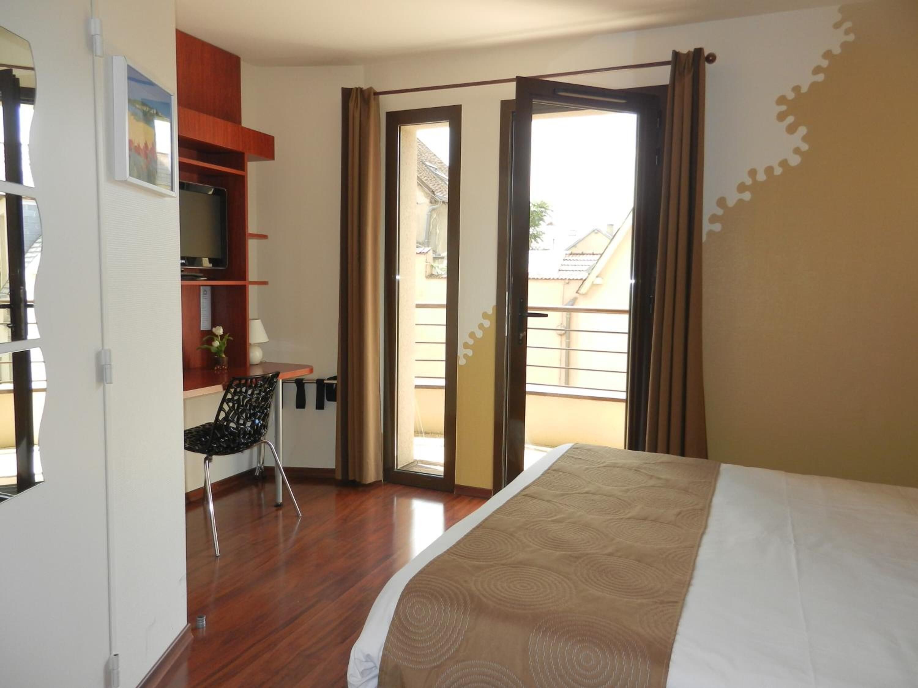 Une chambre d’hôtel comprenant un lit, un bureau avec une chaise, une petite table avec une lampe et une fenêtre avec des rideaux.
