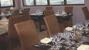 A dining area with tables set for a meal, large windows with a view of a cityscape, and a chandelier on the ceiling. - L'Hôtel (Chartres)