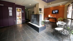 A reception area with a modern design, including a reception desk, seating area, and a television mounted on the wall. - L'Hôtel (Chartres)
