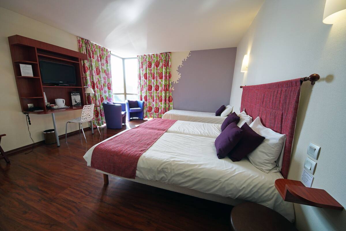 A hotel room with a bed, a desk with a computer, a chair, and a television.