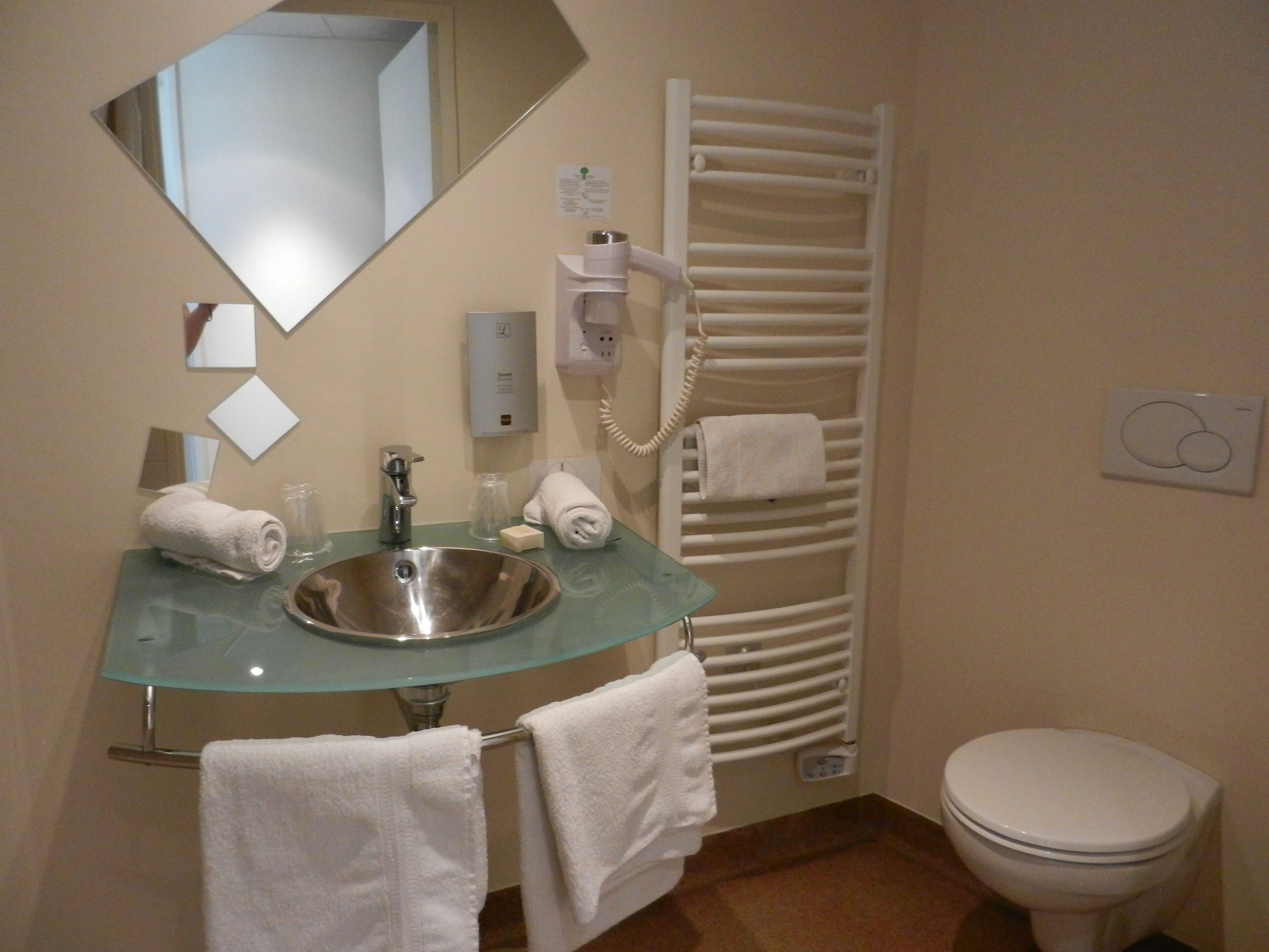 A bathroom with a glass sink, a mirror, a towel rack, a heated towel rail, and a toilet.