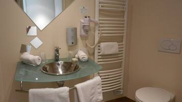 A bathroom with a glass sink, a mirror, a towel rack, a heated towel rail, and a toilet.