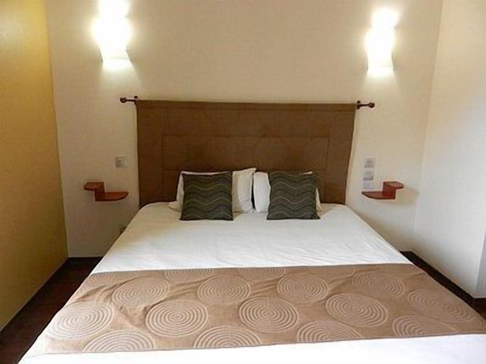 A hotel room with a bed, two pillows, a headboard, and bedside tables.