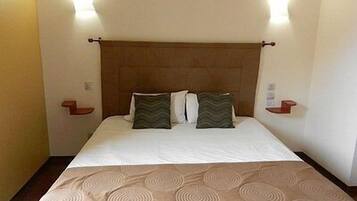 A hotel room with a bed, two pillows, a headboard, and bedside tables.