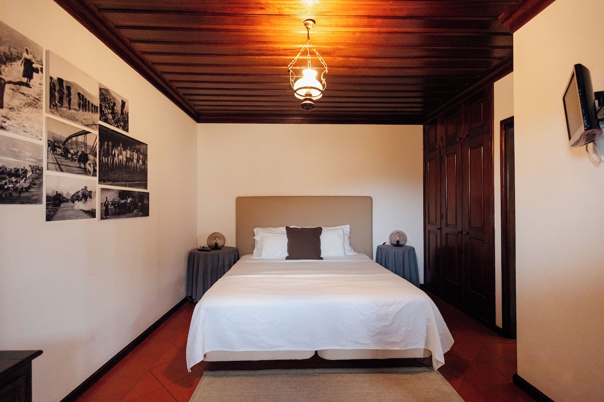 A bedroom with a bed, a wooden ceiling, a wall-mounted light fixture, and a door.